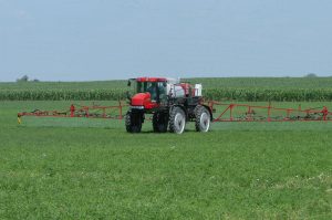 Red crop sprayer driving through a grassy field
